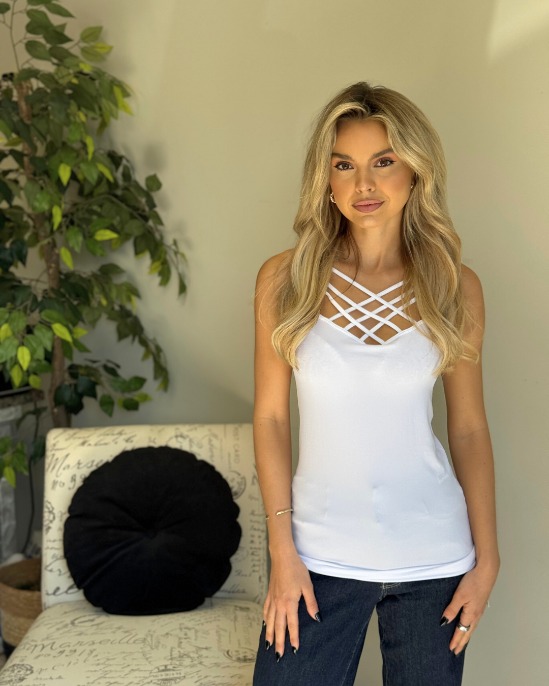 Woman wearing a white tank top with criss-cross design in a casual setting.