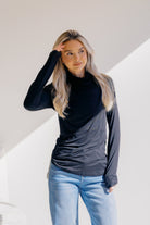 Woman wearing a black long-sleeve top with light blue jeans against a white background