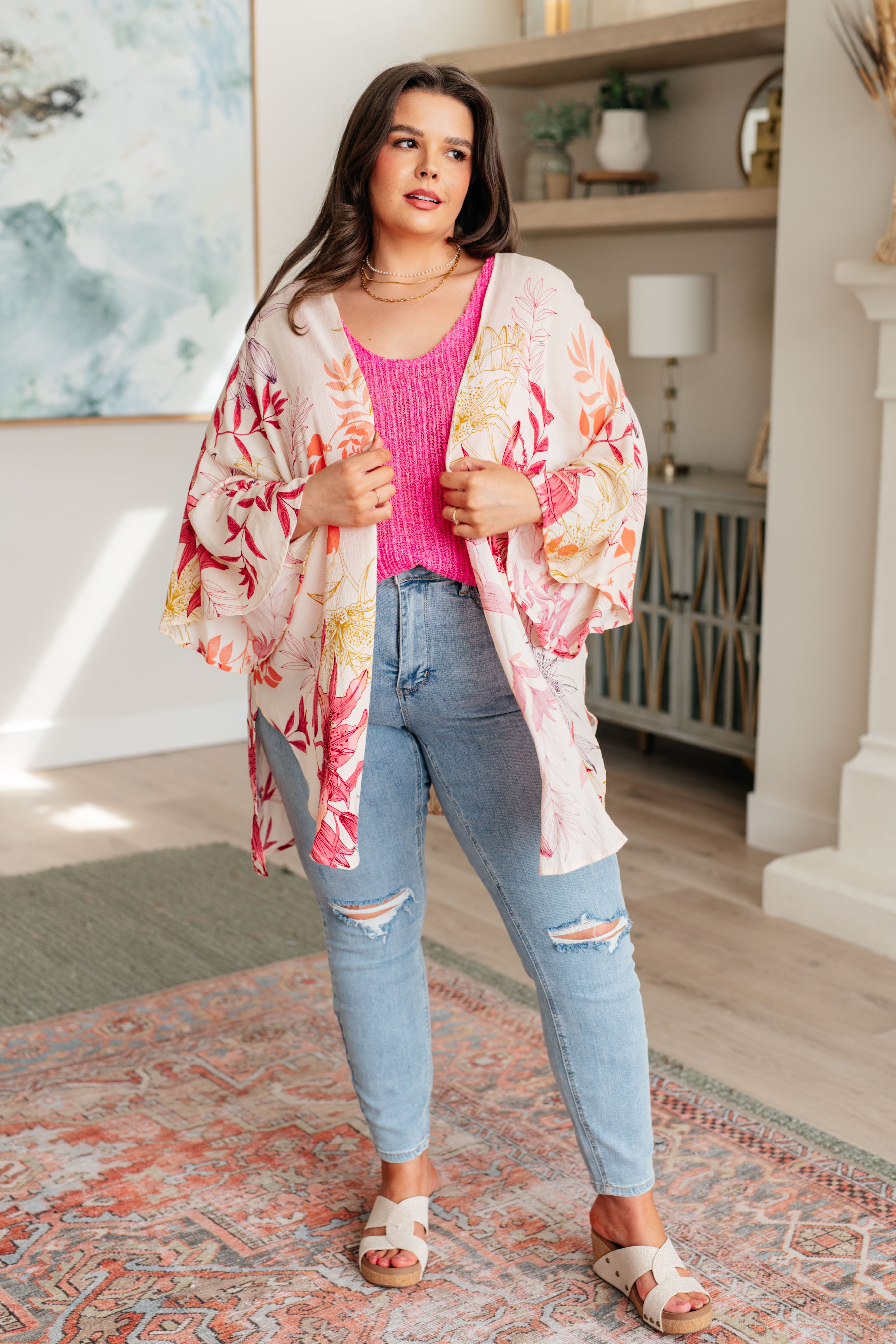 Woman wearing a floral kimono over a pink top and blue jeans in a living room.