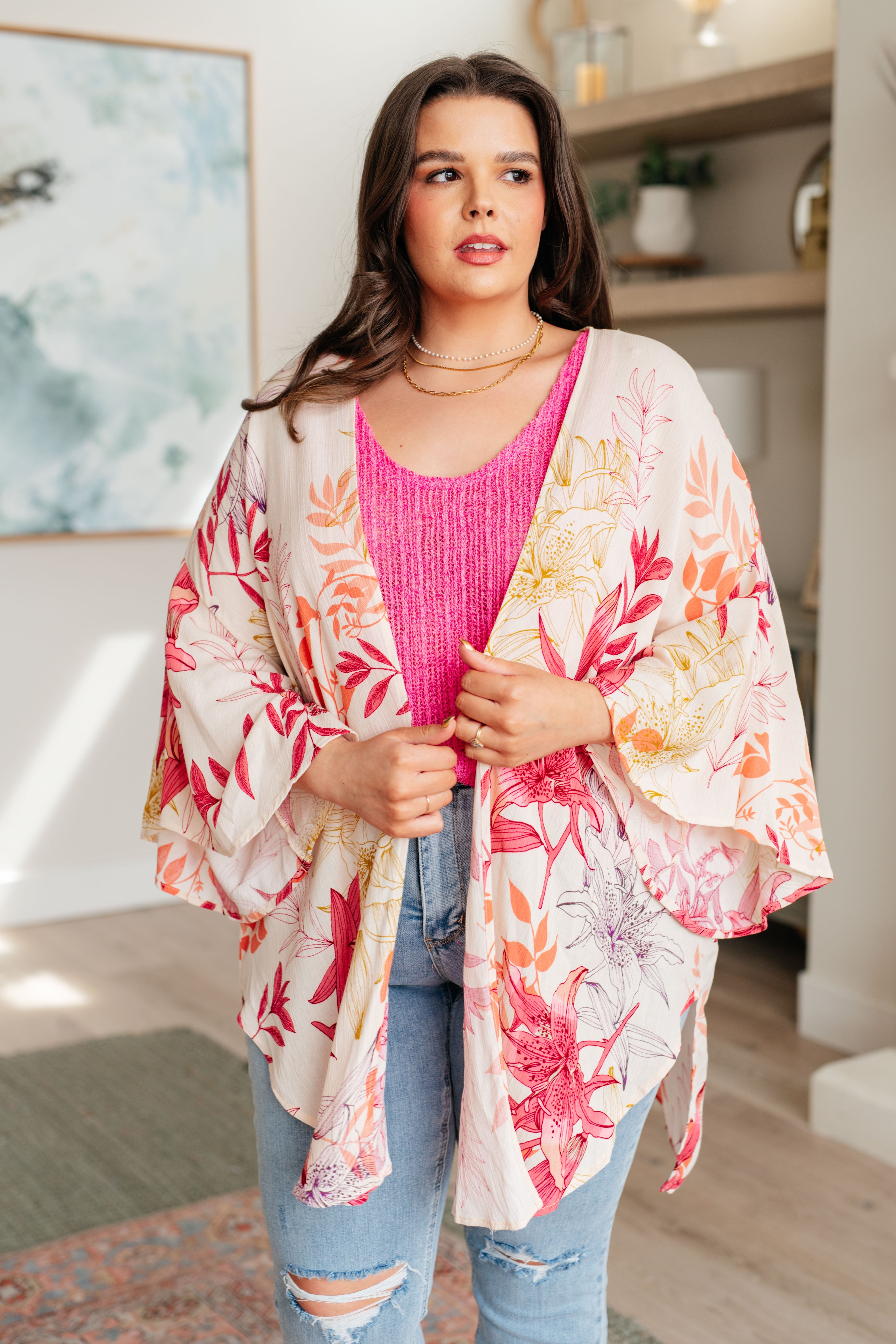 Woman wearing a floral kimono over a pink top and jeans in a room with decor.